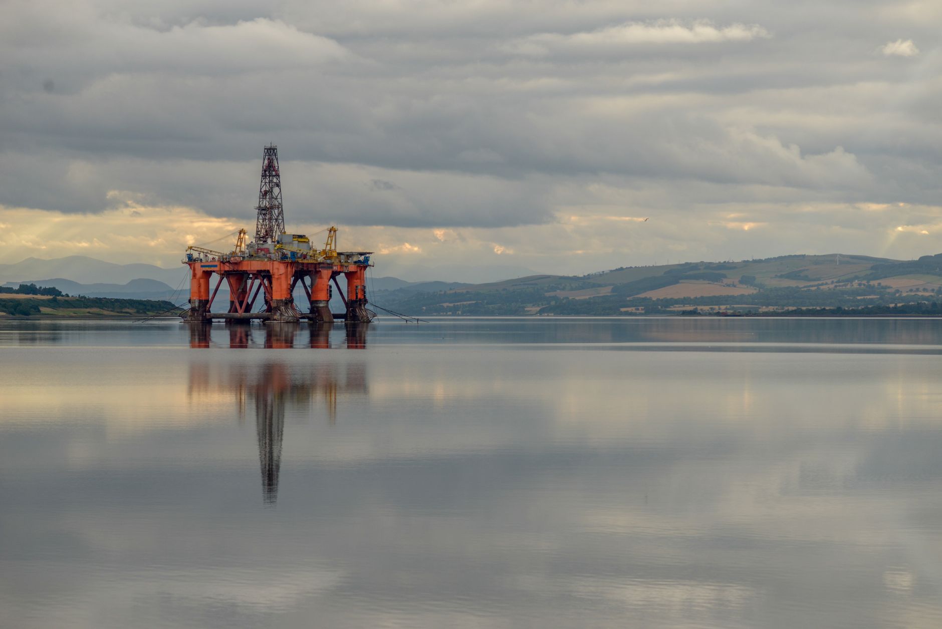A semi-submersible offshore drilling rig moored on calm water under an overcast sky.