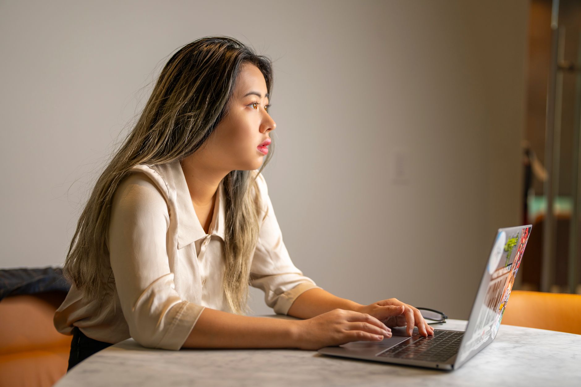 A young woman typing on a laptop at a table indoors.